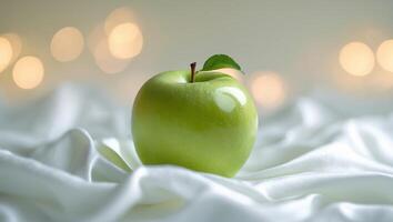 Glowing green apple resting on soft fabric with warm bokeh background in serene setting photo