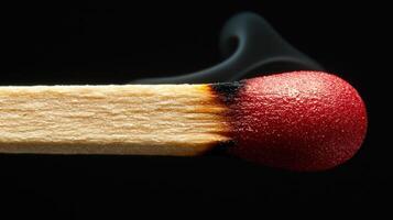 A matchstick is ignited, producing a vibrant flame at its tip. Wisps of smoke rise softly against a dark background, creating an intriguing contrast photo