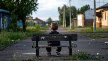 A young boy sits on a bench in an empty street photo