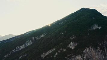 The sun appears from behind a rocky mountain slope overgrown with dense forest. Sunrise in the mountains, aerial view from a drone. Mountain peaks of the Caucasus photo