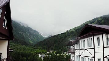 Tourist complex in mountains. The building of hotel at the foot of the rocky mountains, the peaks of which are covered with snow and clouds, filmed from a drone. Mountain nature of the Caucasus photo