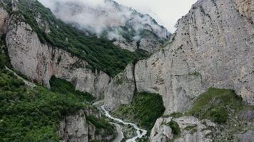 Vertical panning from a quadcopter. A narrow mountain road and a bubbling river in the lowlands between sheer rocky mountains covered with green vegetation and clouds photo