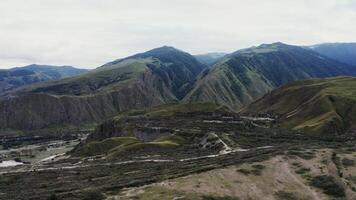 A view of mountain valley with many mountain peaks, slopes are covered with fields and forests. In the lowland one can see a river and a road with cars passing along it. Shooting from a quadcopter photo
