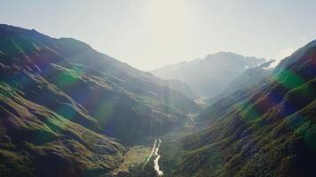 Panoramic shot from a bird's eye view, a view of the mountain valley in the rays of the rising sun. A mountain settlement with a river in the lowland is flooded with sunlight. photo