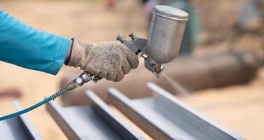 Construction worker painting metal structure surface coating with spray gun at construction site. Metal corrosion and rust protection. Industrial precision. Protective coating to a metal structure. photo