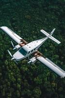 A white airplane with visible wear tear flies over a dense green forest photo