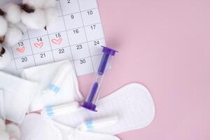 Women's menstrual pads, tampons, female menstruation calendar and alarm clock on a pink background. photo
