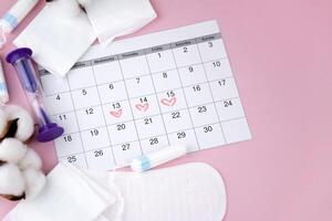 Women's menstrual pads, tampons, female menstruation calendar and alarm clock on a pink background. photo