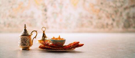 Brass teapot and a bowl of food placed on a table with a decorative wall in the background. photo