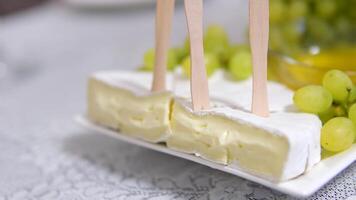 Close up of delicious cheese board with a wheel of camembert, bunch of red grapes and hummus video