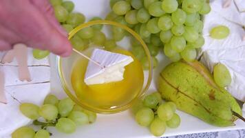 dip brie cheese in honey Cheese plate and Honey. Dips wooden stick to glass bowl with liquid honey, pouring from wooden spoon. Preparation of cheese platter with various types of hard cheese video