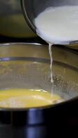 Female hands add milk to bowl of beaten eggs with mixer. Waffle cookie recipe step by step. Hand mixer beats eggs, milk. Beating dough with mixer. Whipping dough for pancakes video