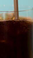 Cola with ice stir with a straw. cocktail or cola stirring into the glass with drinking straw. Bubbles on ice cubes. Gas comes out of the glass, droplets shining in the backlit video