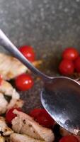 in a frying pan with a spoon stir cherry tomatoes and pieces of chicken meat cook healthy food female hand with red manicure video