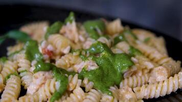 Fusilli pasta cooked with tomatoes and basil in dark gray bowl, rotating isolated on black background, turning, close-up macro. video