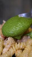 add pesto to pasta. Slow motion add pesto sauce to fusilli pasta in black bowl video