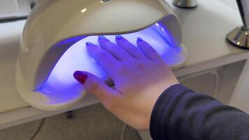 Client placing a hand under a uv lamp for drying nail polish in a beauty salon. Modern equipment provides quick and efficient drying, enhancing the overall manicure process video