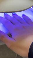Client placing a hand under a uv lamp for drying nail polish in a beauty salon. Modern equipment provides quick and efficient drying, enhancing the overall manicure process video