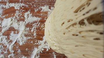 Close-up of airy, well-fermented dough with a porous texture lifted from a floured wooden surface, showcasing gluten development and elasticity in an artisan baking process video