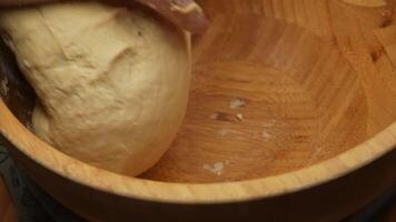 Close-up of tattooed male hands kneading dough in a wooden bowl, fingers covered in flour, veins visible, rustic wooden surface, warm and soft kitchen lighting creating a cozy and homely baking video