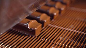 Sweets are poured with chocolate and blown by the airflow. Little waves of chocolate roll along the candies close up. The production line at a candy factory. video