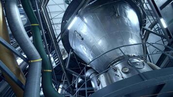 Huge dairy tank beside the thick plastic tubes. Stainless steel tank standing at the raised platform with sensors at its basics. Circle view from below. video