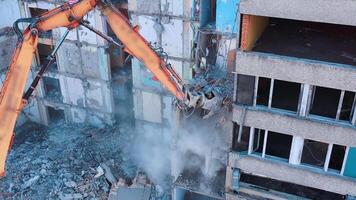 Demolition machine is breaking the floors into pieces and throwing them down. Powerful claw of excavator demolishing the ruined building. video