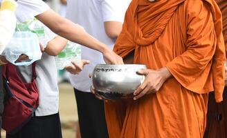 A monk is holding a silver bowl and giving it to a person photo