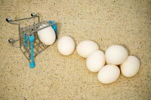 Small shopping cart tipped over with eggs spilling out on surface photo