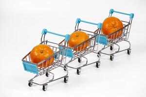 Three miniature shopping carts with oranges lined up on a white surface photo