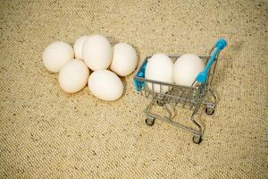 Small shopping cart with eggs next to a larger pile on fabric photo