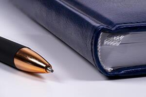 Close-up of a blue notebook and a black pen on a white surface photo