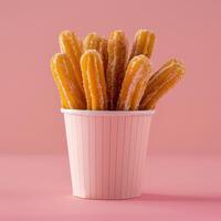 Delicious crispy churros in a pink striped paper cup on a pink background photo