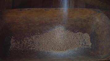 The ancient Quern stone hand mill with grain. The man grinds the grain into flour with the help of a millstone. Men hands on a millstone. Old grinding stones turned by hands video