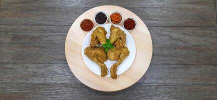 Ayam ungkep bumbu kuning or boiled chicken with curry seasoning and coconut water. Served with varian sambal or hot chili sauce. Ready to fried photo