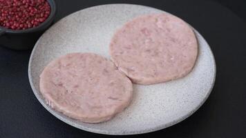 Raw chicken burger cutlet with salt, spices and herbs on dark concrete background video