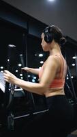 Middle-aged woman running on a treadmill, elliptical trainer in health club. A fit girl dressed in sports outfit, doing cardio cross training on a cross-trainer. Doing warm-up before training session video