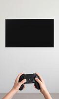 Blank TV mounted on a wall with a gamepad in hands, vertical composition, ideal for promoting games and immersive home entertainment setup photo