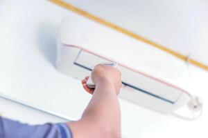 A person using a remote control to adjust an air conditioning unit mounted on the wall. photo