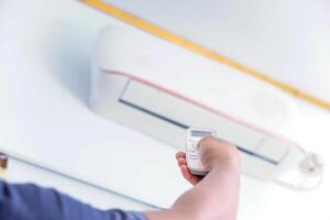 A person using a remote control to adjust an air conditioning unit mounted on the wall. photo