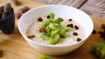 cooked oatmeal with kiwi, honey and nuts in a bowl on a wooden table video