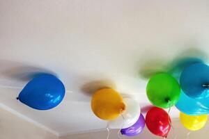Group of multicolored vibrant helium balloons with ribbons in red, blue, yellow, green, purple, and white hanging from a ceiling, perfect for party themes or event decorations. 3 photo