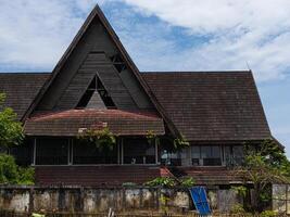An abandoned two stories convention hall with traditional architecture with overgrown fern and broken windows and tiles shot from low angle in a sunny day photo