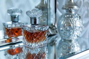A bottle of perfume sits on a table next to a mirror photo