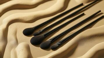 A set of five black makeup brushes lays on a wavy textured surface, showcasing their elegant design. The arrangement highlights both functionality and aesthetic appeal in a beauty context photo