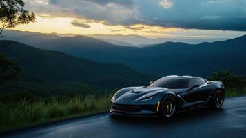 A sleek black sports car is parked alongside a winding mountain road. The sun sets behind distant peaks, casting warm hues over the landscape and creating a moody atmosphere with dark clouds photo