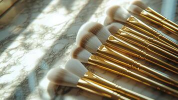 A collection of makeup brushes lies flat on a marble surface, showcasing their elegant gold handles and soft bristles. Natural light highlights the textures and materials photo