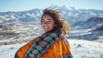 A woman smiles while wearing a colorful blanket on top of a mountain photo