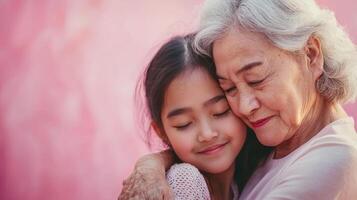 A joyful grandma and her granddaughter share a tender hug, closing their eyes in contentment. The soft pink backdrop enhances the warmth of the moment, embodying affection and connection photo