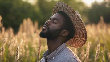 A young man enjoys a peaceful moment in a golden field at sunset, wearing a straw hat and closing his eyes. The warm glow of dusk creates a serene atmosphere photo